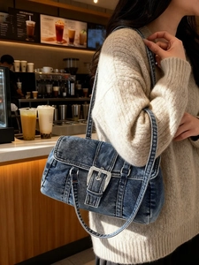 Sac Boston en jean rétro avec boucles argentées porté à l'épaule dans un café chic