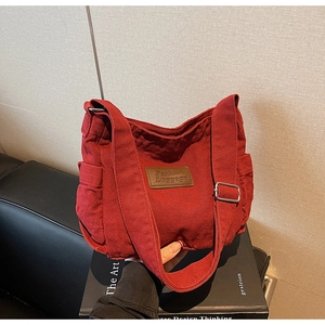 Detail of red canvas tote bag with brown leather label and wide adjustable shoulder strap