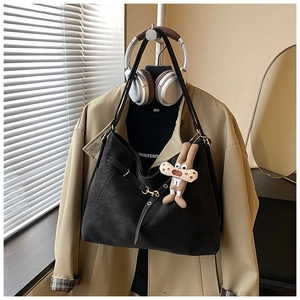 Detail of black tote bag with buckle straps and a brown doll charm on a mannequin