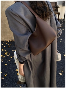 Detail of dark brown lychee grain leather hobo bag worn by a model in a gray blazer