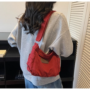 Detail of red canvas tote bag with brown leather label and side pocket worn by a model