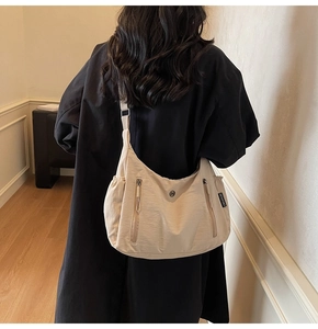 Détail d'un sac bandoulière en nylon beige avec fermetures éclair porté par un mannequin