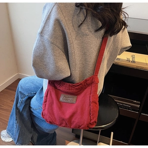 Close-up of a red canvas tote bag featuring a leather patch and pleated side pockets