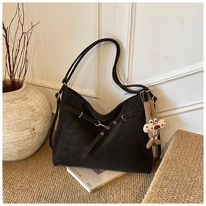 Detail of black matte leather shoulder bag with gold hardware and cartoon charm