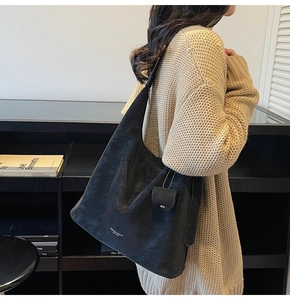Detail of a large black matte hobo bag worn over the shoulder with wide strap