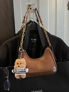 Vintage brown suede crossbody bag with gold chain strap and bear charm on black suit