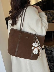 Large dark brown suede tote bag with bear charm shown on model in cream coat
