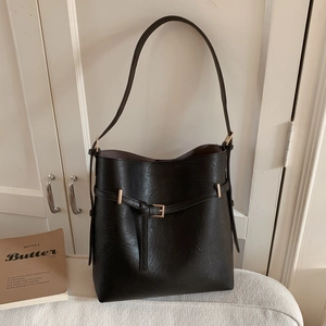 Detail of black leather bucket bag with litchi grain and gold buckle on cabinet