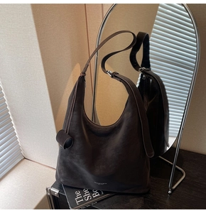 Detailed view of large dark brown hobo bag with smooth texture on a black surface