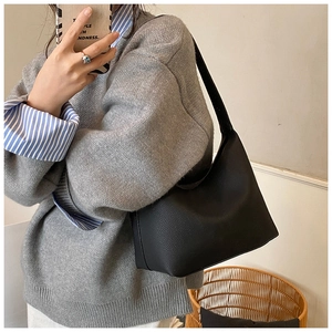 Detail of black pebbled leather texture on a large capacity tote bag worn as a shoulder bag