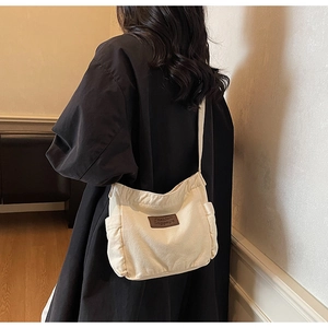 Detail of off-white canvas tote bag with side pockets and leather logo on black coat