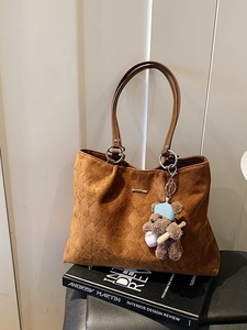 Brown woven suede tote bag with teddy bear charm on designer book stand for daily commute