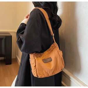 Detail of the orange canvas tote bag with brown leather logo patch and wide strap