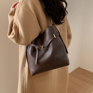 Detail of dark brown leather bucket bag with adjustable strap and golden buckle on model