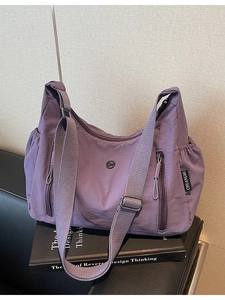 Sac bandoulière violet en nylon avec poches multiples sur canapé en cuir