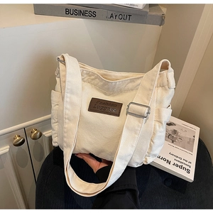 Detail of off-white canvas tote bag featuring adjustable shoulder strap and brown leather patch
