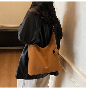 Side view of a large brown leather shoulder bag worn by a model in a black jacket