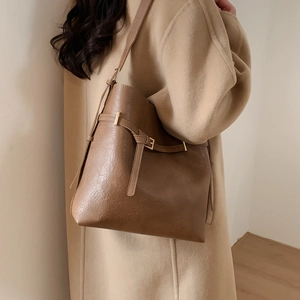 Detail of dark brown leather bucket bag showing wide strap and metallic buckle texture