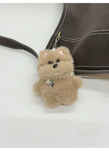 Close-up of a plush dog bag charm with pearl necklace and metal bone pendant on leather bag