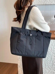 Grand sac fourre-tout noir avec larges bandoulières porté par un mannequin dans un décor épuré
