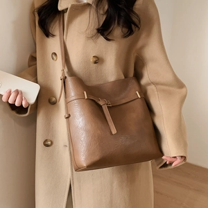 Detail of dark brown leather bucket bag with gold hardware worn with a beige coat