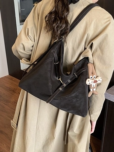 Minimalist vintage dark brown leather tote bag with decorative straps and plush charm on trench coat