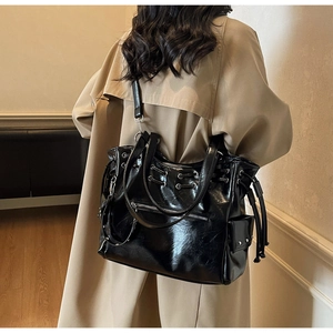 Détail du grand sac cabas noir brillant avec boucles argentées sur trench-coat