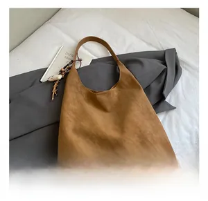 Detail showing the dark brown suede tote bag texture with shell charm and woven pendant