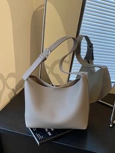 Minimalist grey pebbled leather tote bag with adjustable strap on a reflective surface