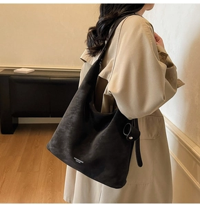 Detail of a black leather tote bag with side buckle decoration on a beige coat background