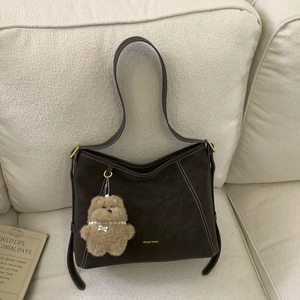 Detail of dark brown matte tote bag featuring contrast stitching and a plush bear charm