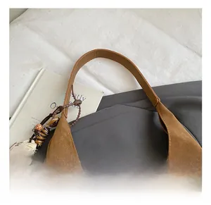 Detail of soft brown suede shoulder bag featuring reinforced leather handle and woven charm