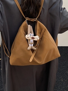 Minimalist dark brown leather backpack with cute plush rabbit charm on a stylish blazer