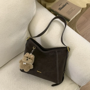 Detail view of vintage brown bucket bag with white stitching and plush bear charm