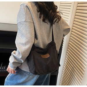 Detail view of black canvas tote bag with side pocket and brown leather label