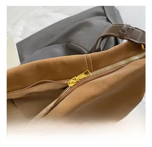 Détail de la fermeture éclair dorée et du daim marron sur un sac à main fourre-tout