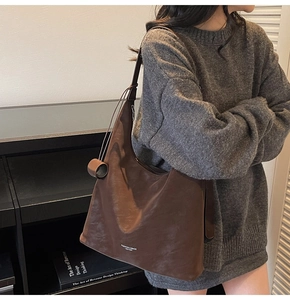 Close-up of brown leather tote bag with wide strap and side tassel decoration
