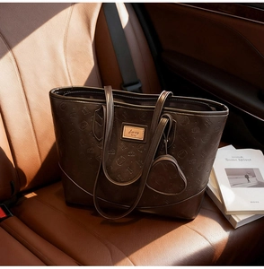 Close-up of embossed dark brown leather tote bag with heart charm and gold nameplate