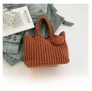 Detail of brown chunky knit handbag featuring a round charm with a Hand Made leather tag