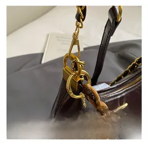 Macro detail of dark brown leather crossbody bag with gold chain and plush charm