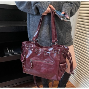 Détail d'un grand cabas rouge foncé avec cordons latéraux et rivets métalliques