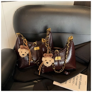 Close-up of wine red quilted bag with gold chain and plush bear charm on black leather