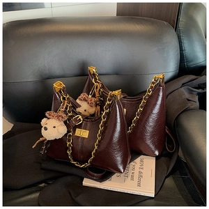 Detail of a brown leather handbag with gold chain strap and cute bear charm on a sofa