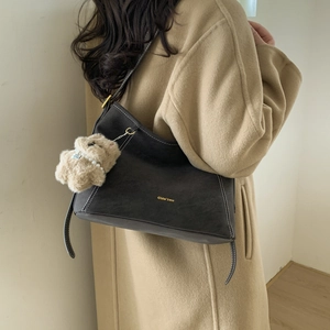 Detail of vintage brown suede shoulder bag with white contrast stitching and plush charm
