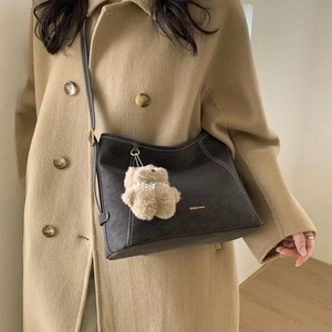 Detail of dark brown tote bag with contrast stitching and plush bear charm on a model