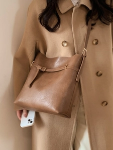 Brown faux leather bucket bag with gold hardware worn by a model in a wool coat