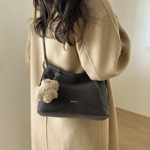 Detail of dark brown suede bucket bag with contrast stitching and teddy bear charm