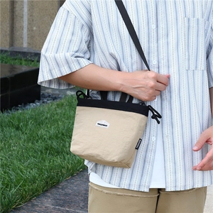 Detail of a beige nylon crossbody bag with black drawstring closure and fashion label