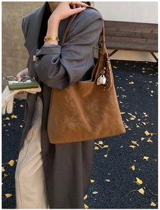Detailed view of a brown suede tote bag with a coffee cup charm on an autumn street