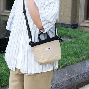 Detail of a two-tone nylon crossbody bag featuring a black and khaki canvas patchwork design
